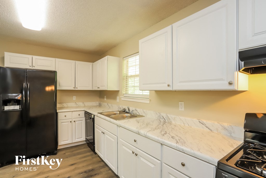 a kitchen with white cabinets and marble counter tops and a black refrigerator