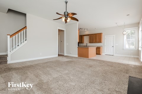 an empty living room with a ceiling fan and a kitchen