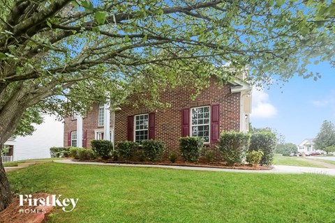 the front of a brick house with a lawn and a tree