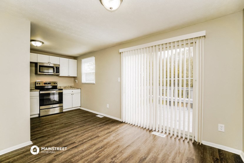 an empty living room with a large white blind door and a kitchen