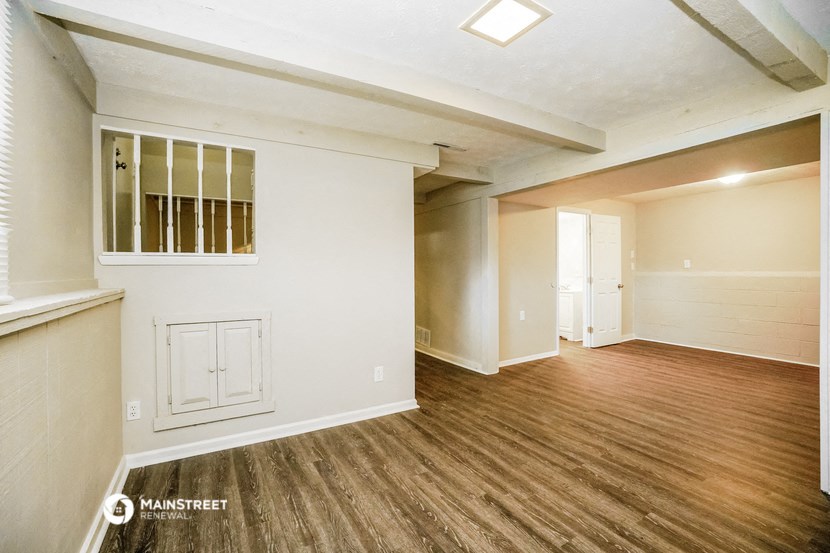 the living room and dining room of an apartment with wood flooring and white walls
