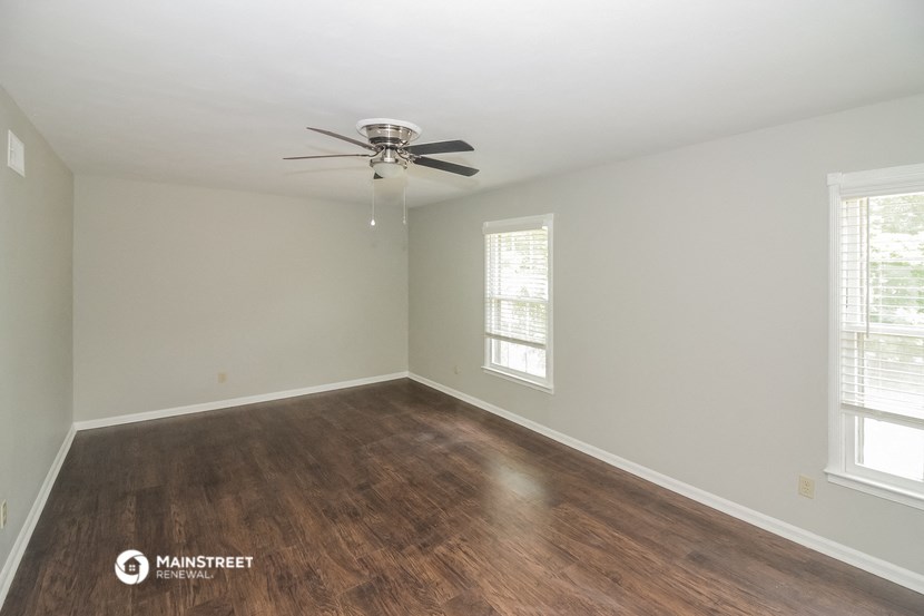 the spacious living room with hardwood flooring and a ceiling fan