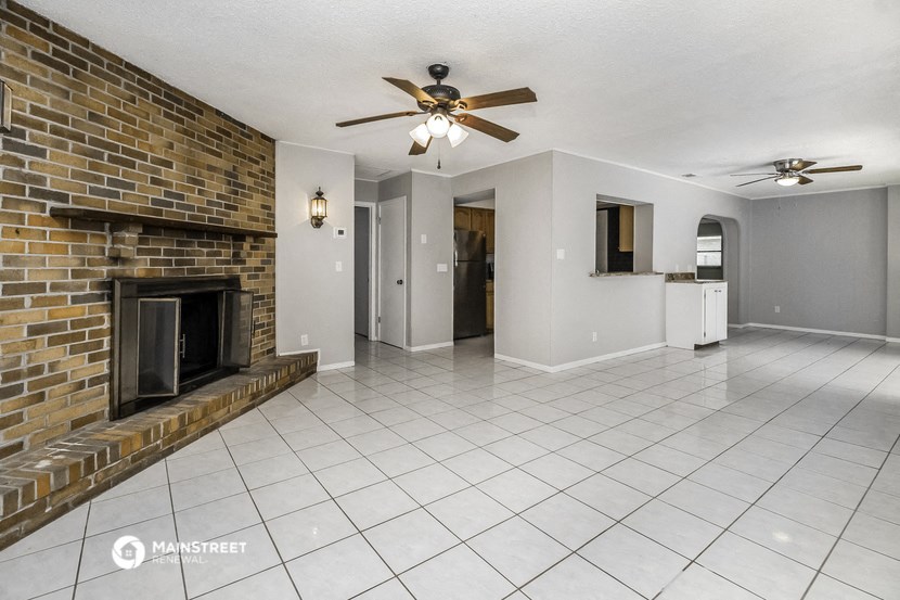 an empty living room with a brick fireplace and a ceiling fan