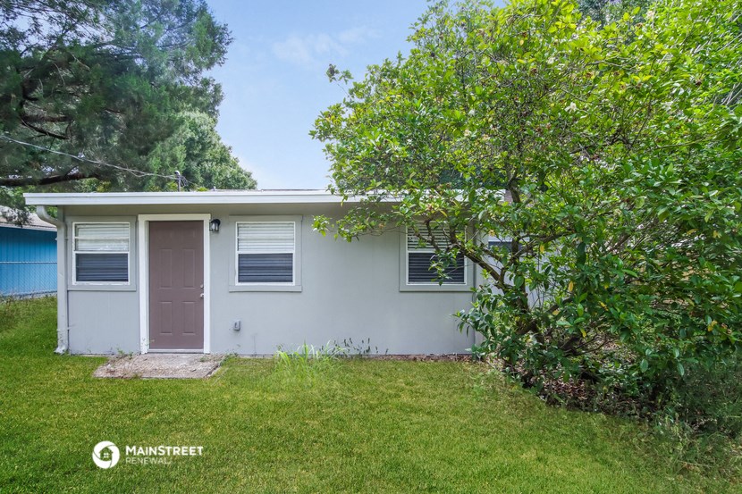 a small white house with a pink door and a tree
