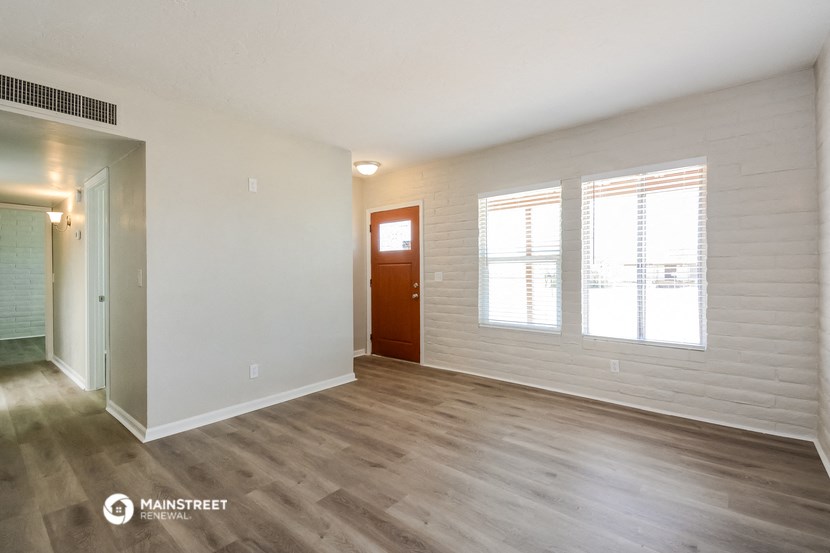 the living room of an apartment with white walls and wood flooring
