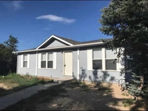 a small white house with a driveway and trees