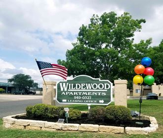 a sign for wildwood apartments with balloons and an flag