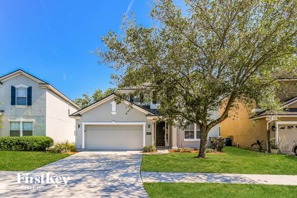 a white house with a tree in the yard and a driveway