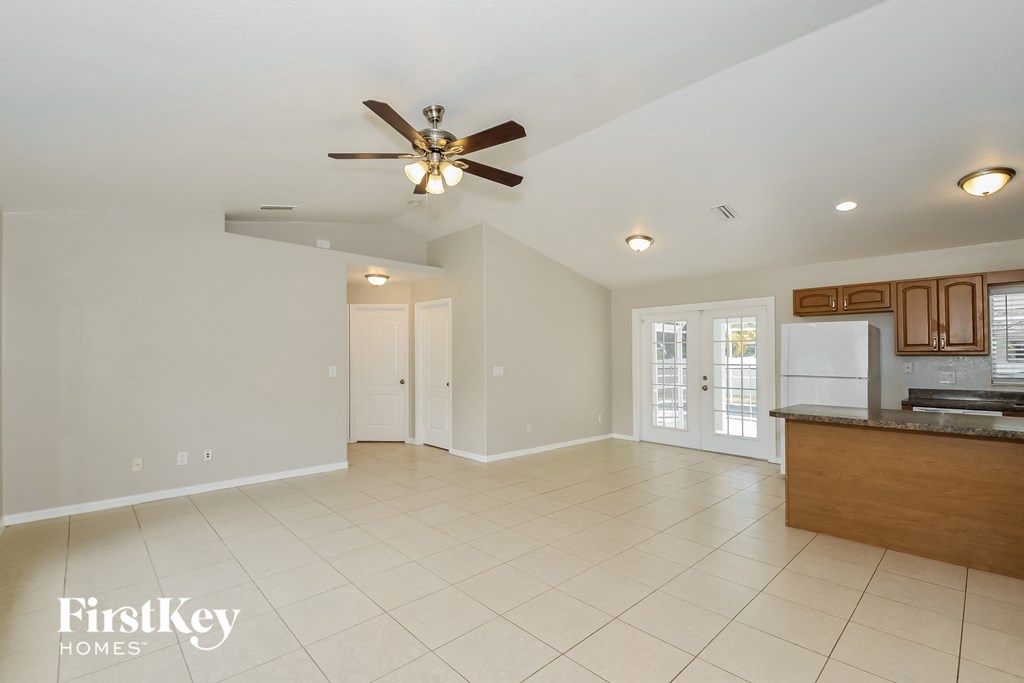 A spacious living room with a ceiling fan and a kitchen area in the background.