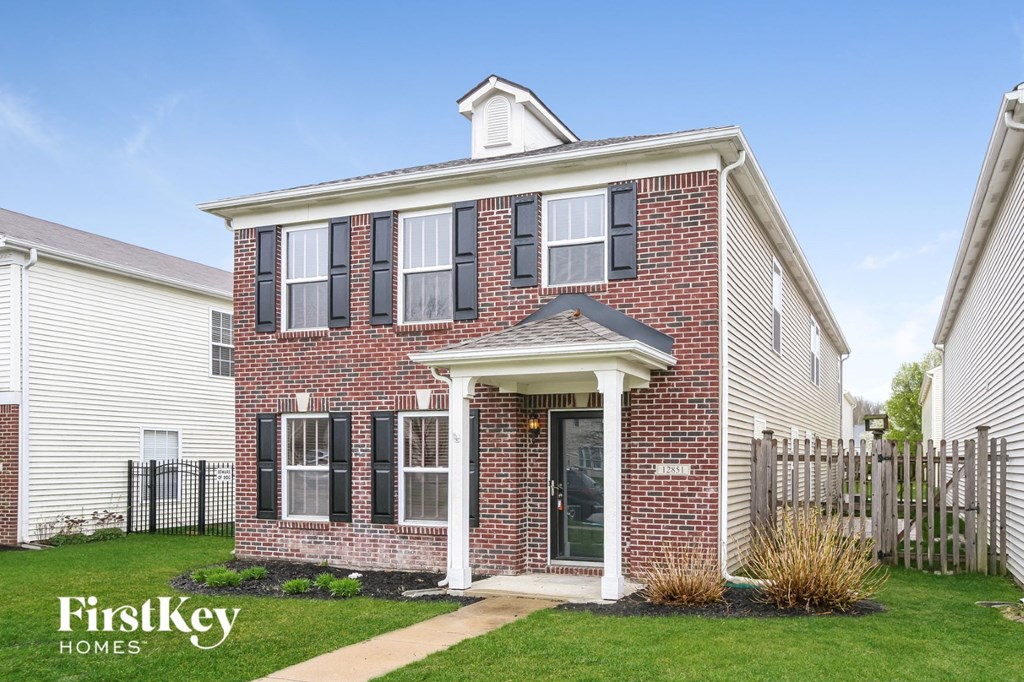 the front of a brick house with a lawn and a wooden fence