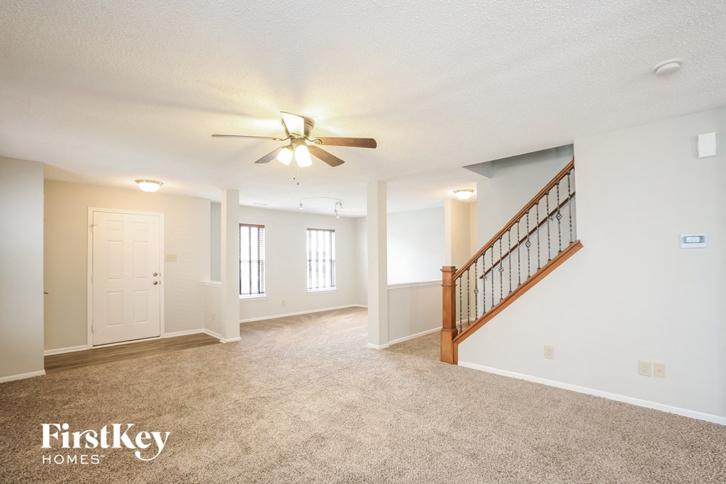 an empty living room with a ceiling fan and a staircase