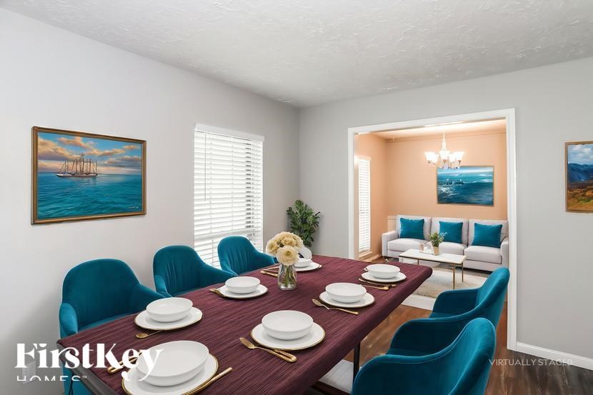 A dining room with a table set for six and a painting of a sailboat on the wall.