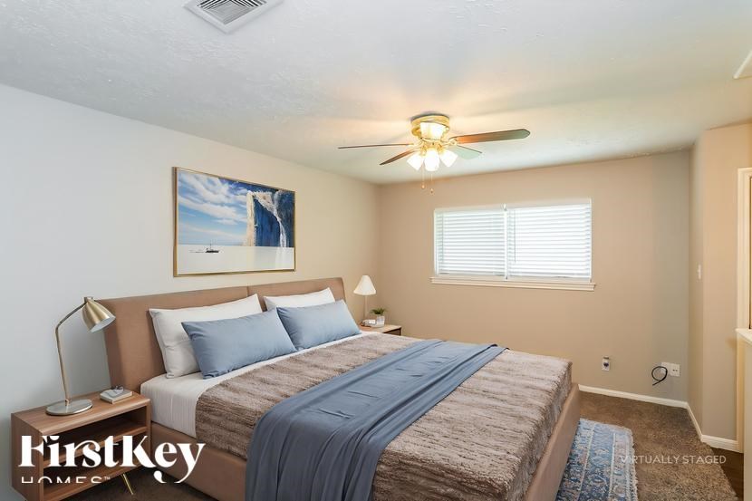 A bedroom with a bed, pillows, a ceiling fan, and a painting on the wall.
