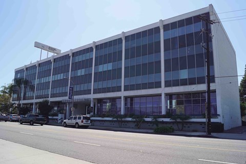 A large building with a lot of windows is on the corner of a street.