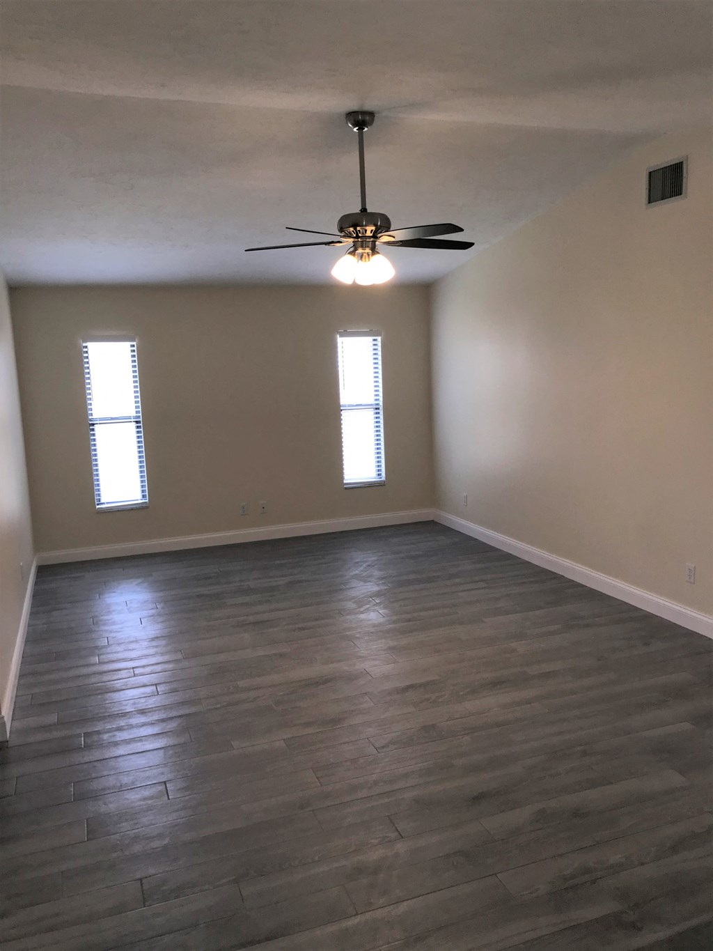 an empty living room with wood floors and a ceiling fan
