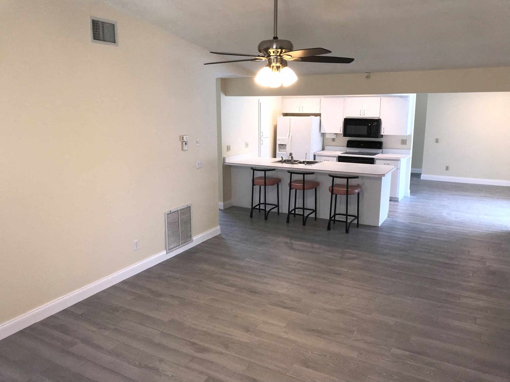 an empty living room with a kitchen and a ceiling fan