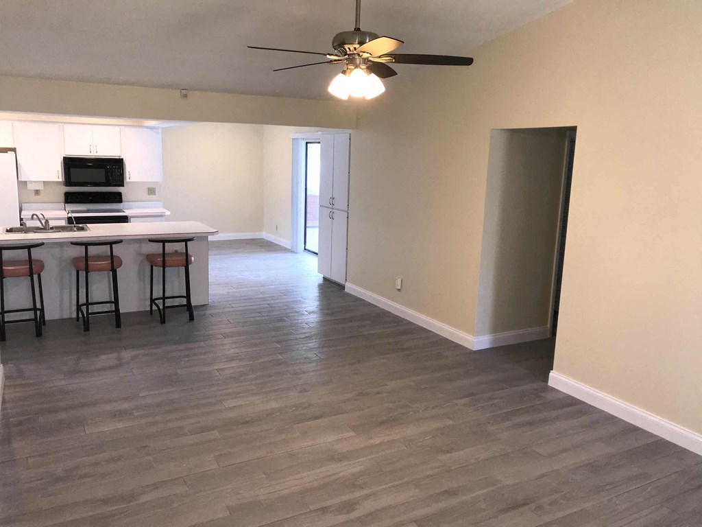 an empty living room with a kitchen and a ceiling fan