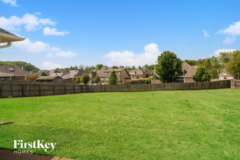A grassy field with a fence and houses in the background.