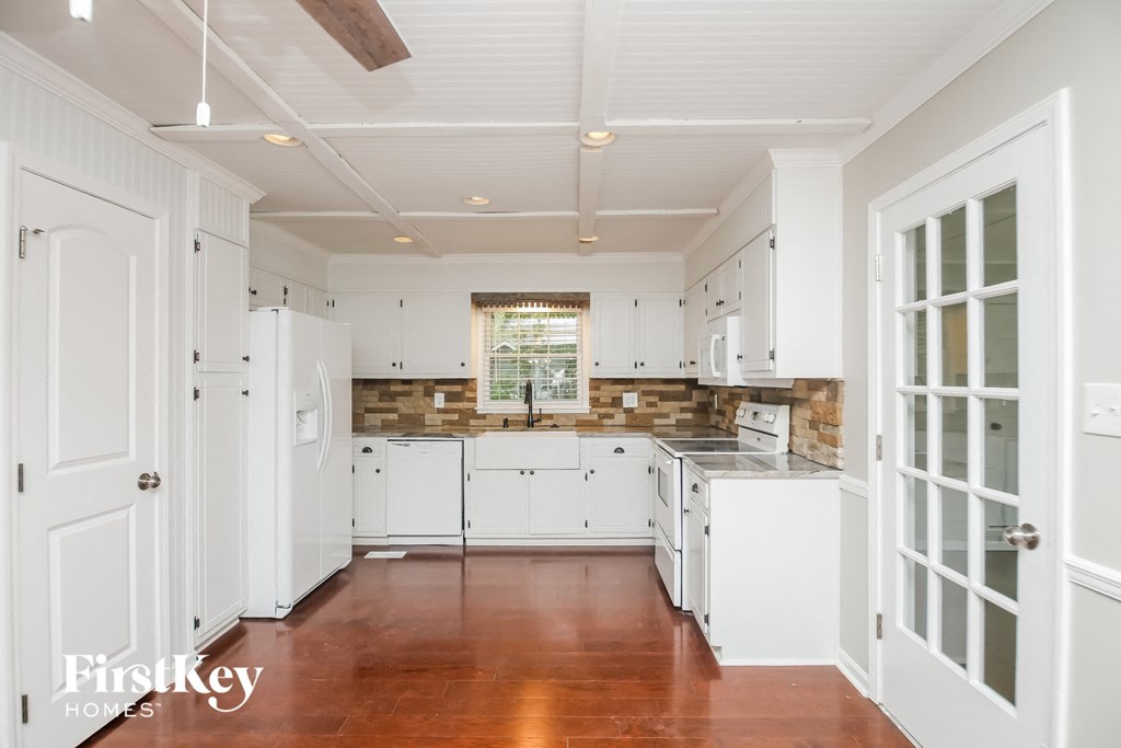 a kitchen with white cabinets and white appliances and wood floors