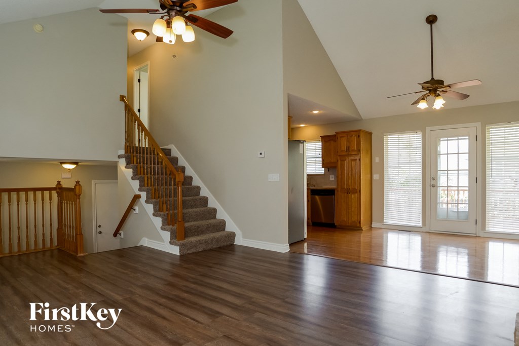 A spacious living room with a staircase and a ceiling fan.