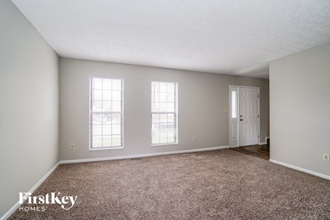 a spacious living room with carpet and two windows