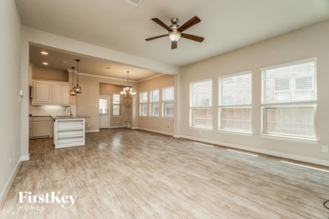 an empty living room with a ceiling fan and a kitchen