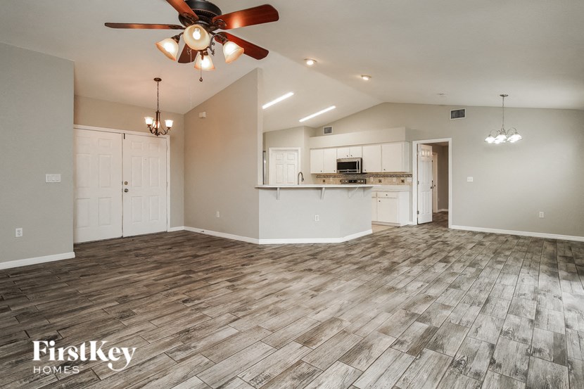 an empty living room with a ceiling fan and a kitchen