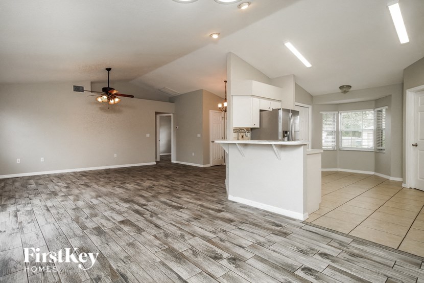 an empty living room with a kitchen and a ceiling fan
