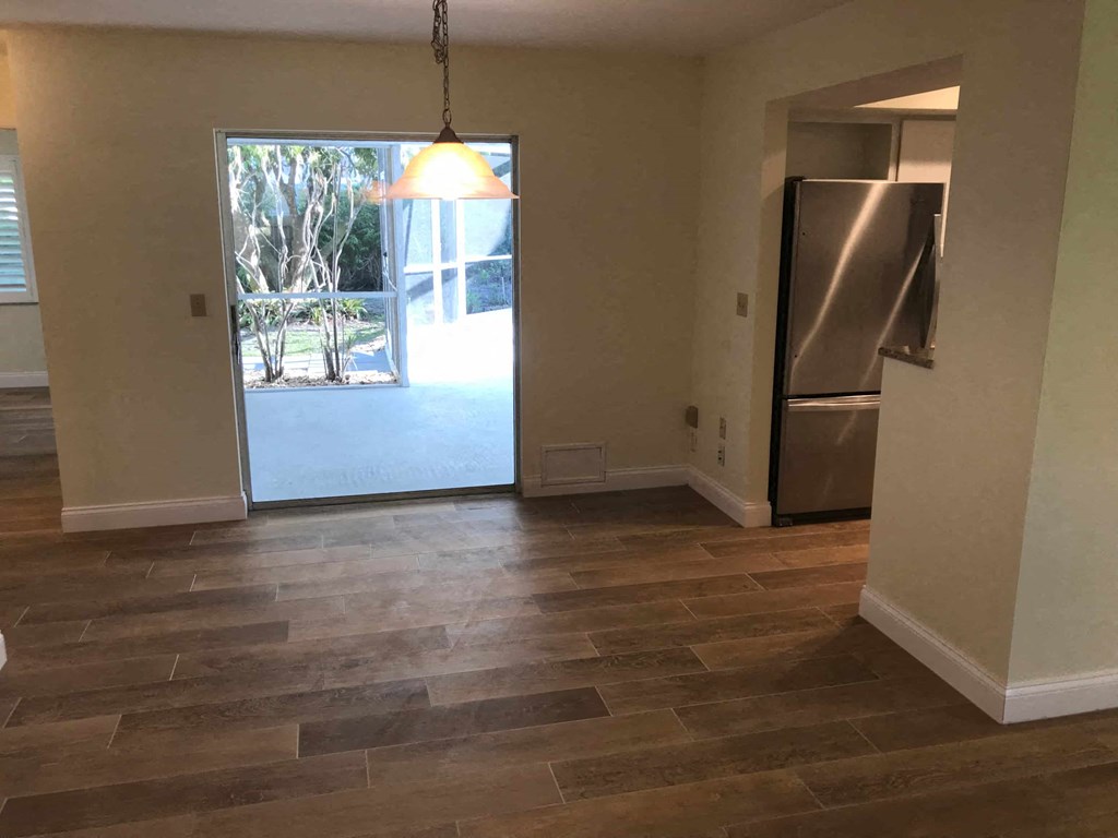 an empty living room with a refrigerator and a door to a patio