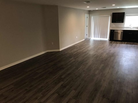 A room with wooden flooring and a kitchen area in the background.