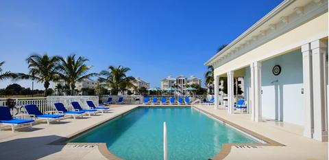 a swimming pool in front of a house with blue chairs