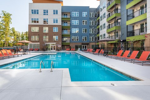 a swimming pool with orange chairs and an apartment building in the background