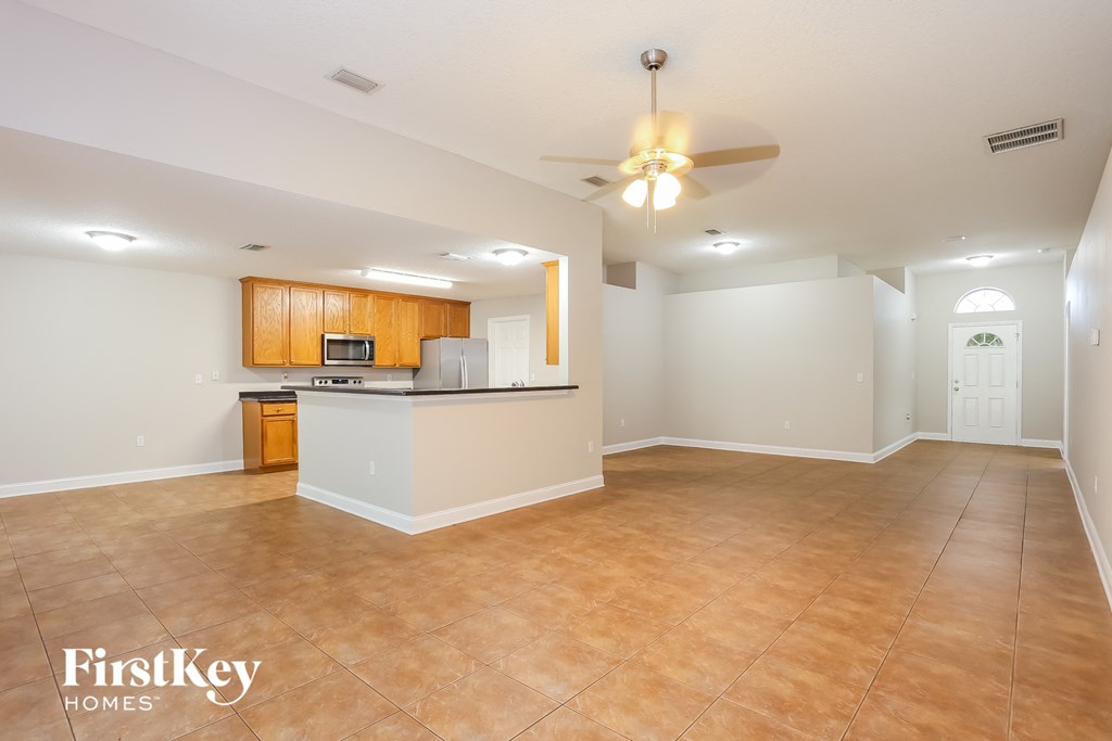 an empty living room with a kitchen and a ceiling fan