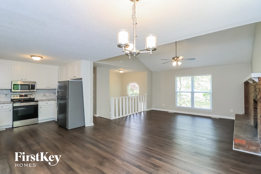 A well-lit, spacious kitchen and living room with wooden floors and a chandelier.