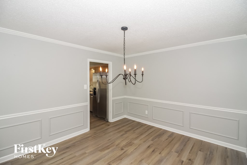 A chandelier hangs over a white-walled room with wood flooring.