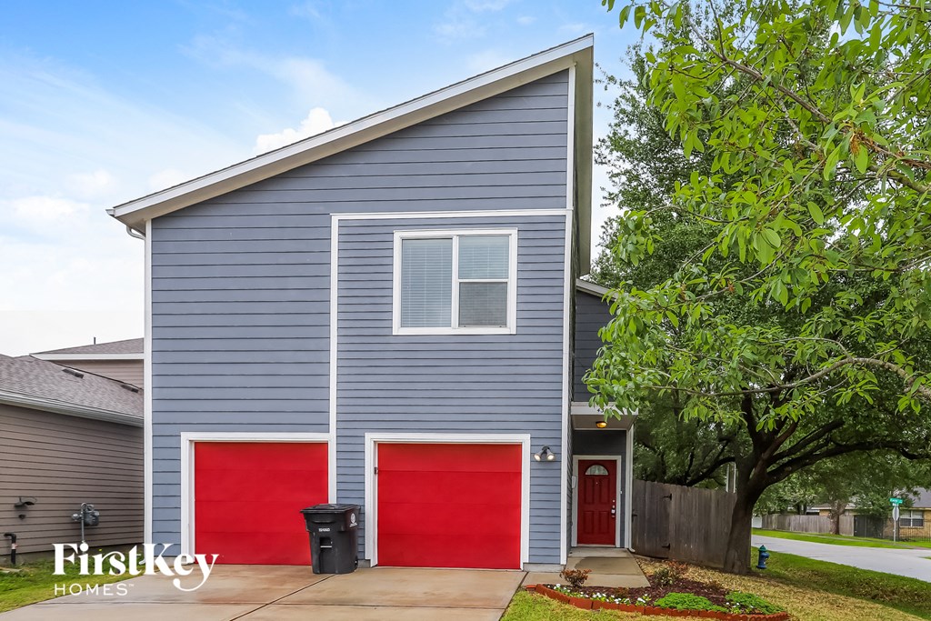 A grey house with red garage doors and a black trash bin in front.
