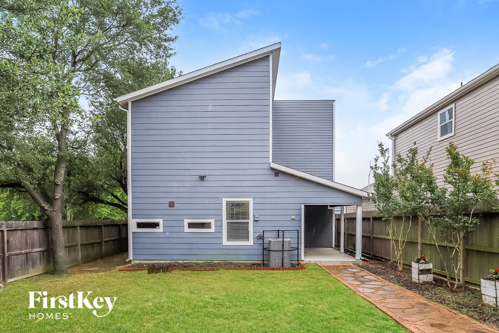 A modern house with a grey exterior and a white window is surrounded by a wooden fence and a green lawn.