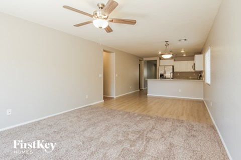 A spacious room with a ceiling fan and a kitchen area in the background.