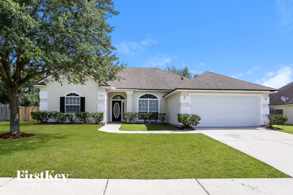 A white house with a brown roof and a tree in front.