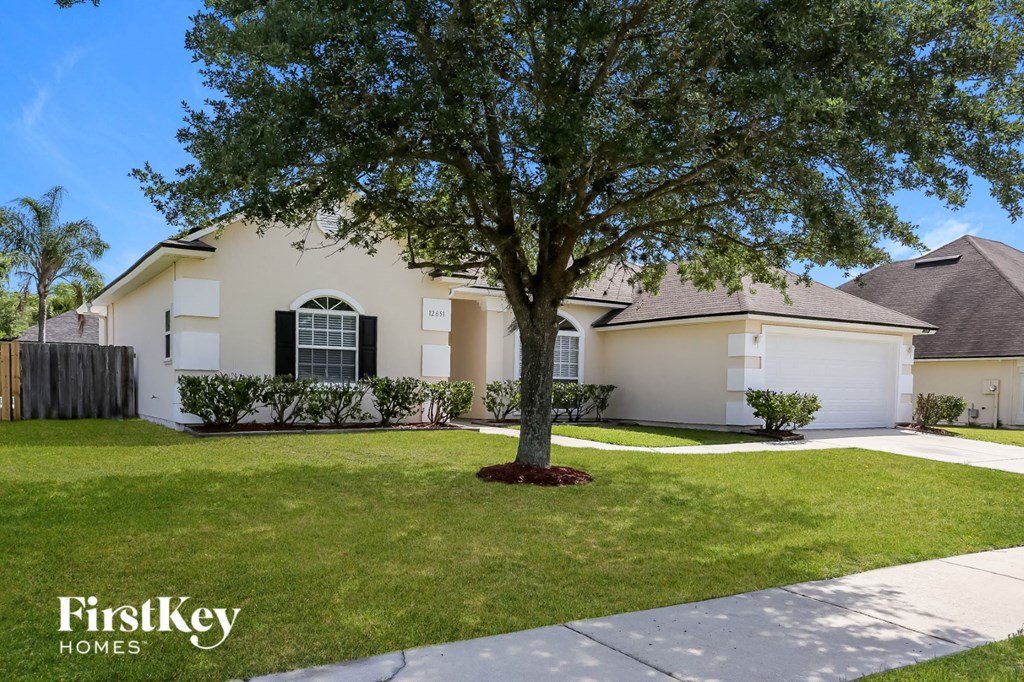 A tree stands in front of a white house with a sign that says FirstKey Homes.