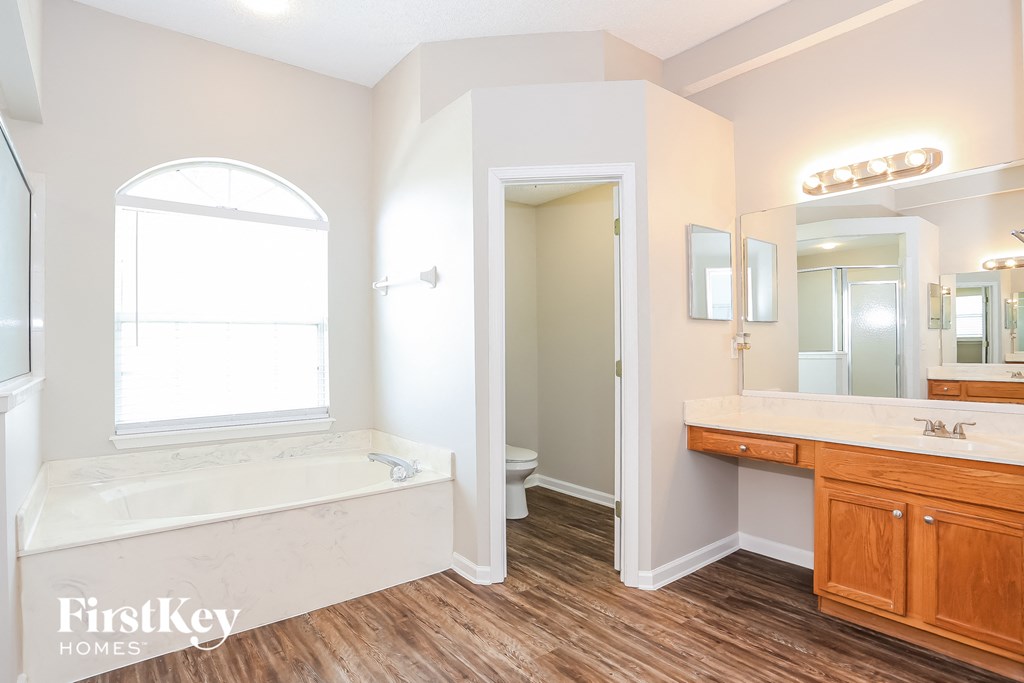 A bathroom with a tub, sink, mirror, and wooden floors.