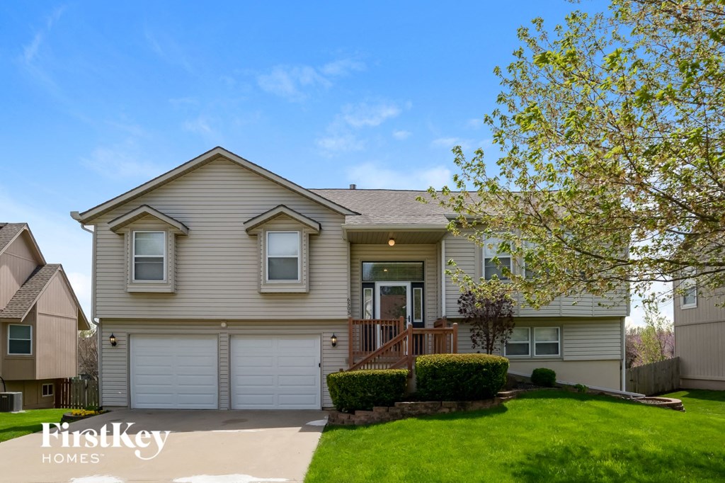 a beige house with white garage doors and a green lawn