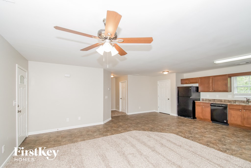 a empty living room with a ceiling fan and a kitchen