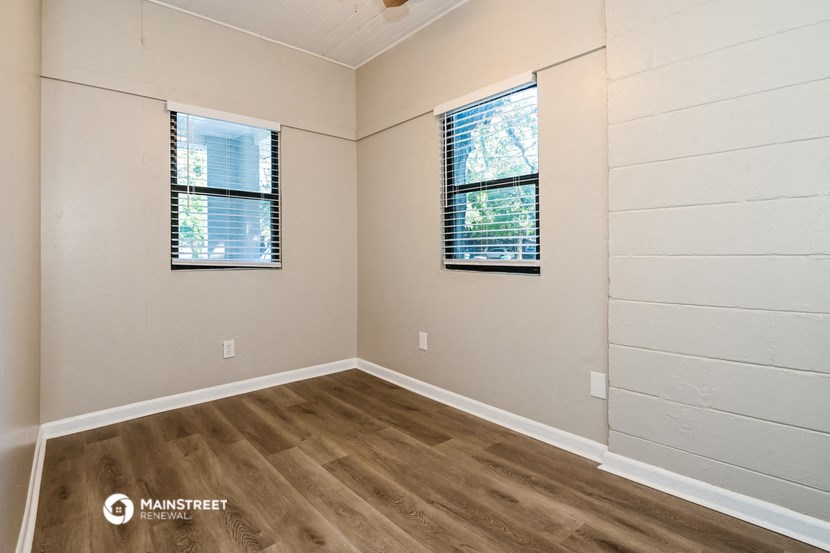 the interior of an empty room with wood flooring and two windows