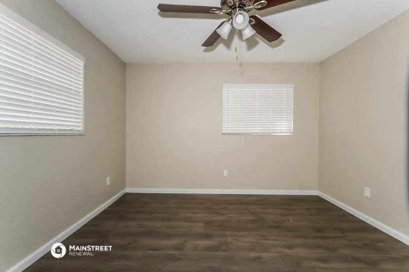 a empty living room with a ceiling fan and two windows