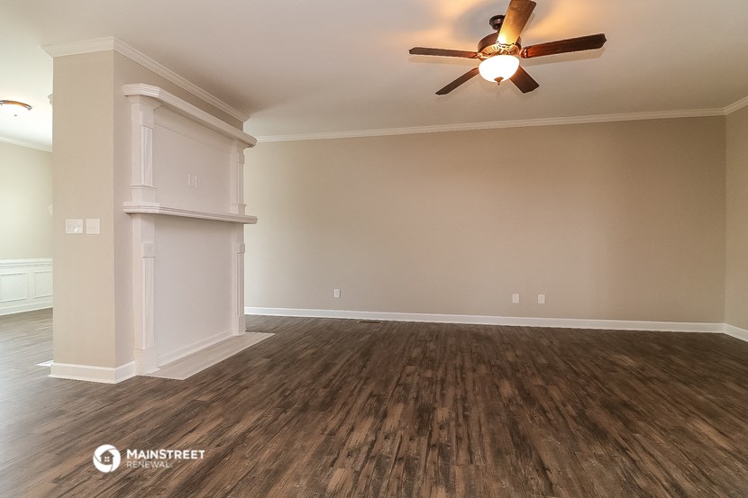 the spacious living room with hardwood flooring and a ceiling fan
