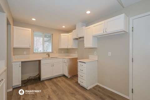 the kitchen of a home with white cabinets and white counter tops and a wooden floor