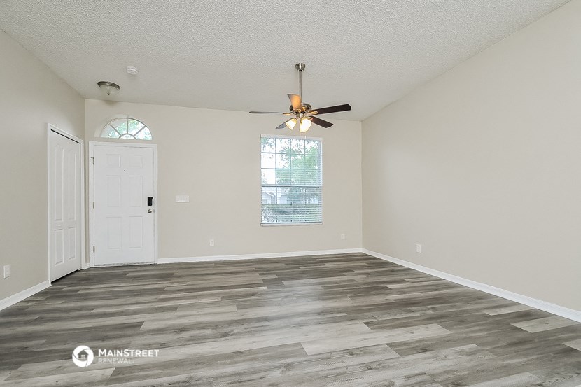 an empty living room with a ceiling fan and a door