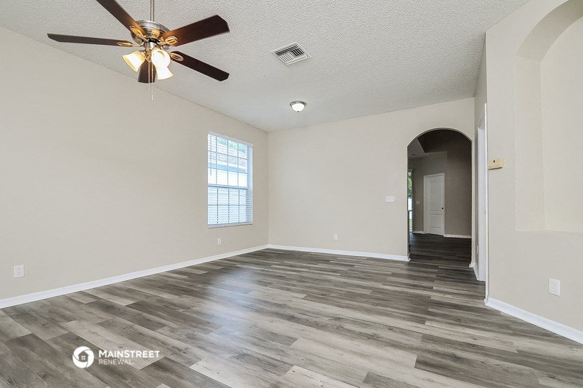 the spacious living room with hardwood flooring and a ceiling fan