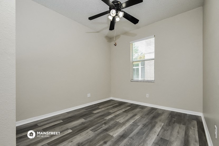 the spacious living room with wood flooring and a ceiling fan